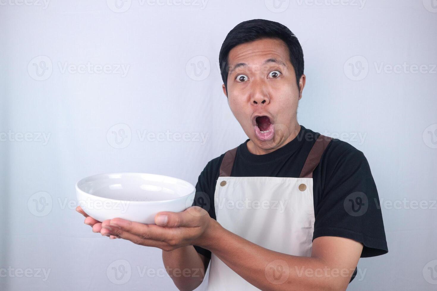 Shocked face expression asian man chef or waiter shows empty white bowl, presenting something. photo