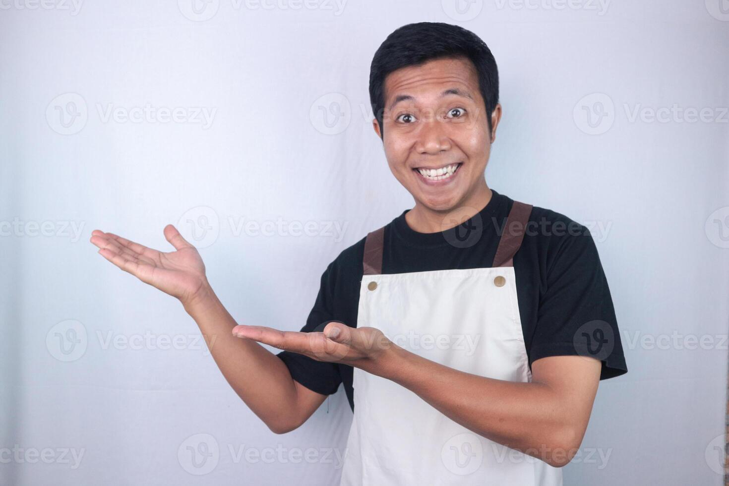 Smiling face expression young asian man wearing apron pointing right side, empty space. photo