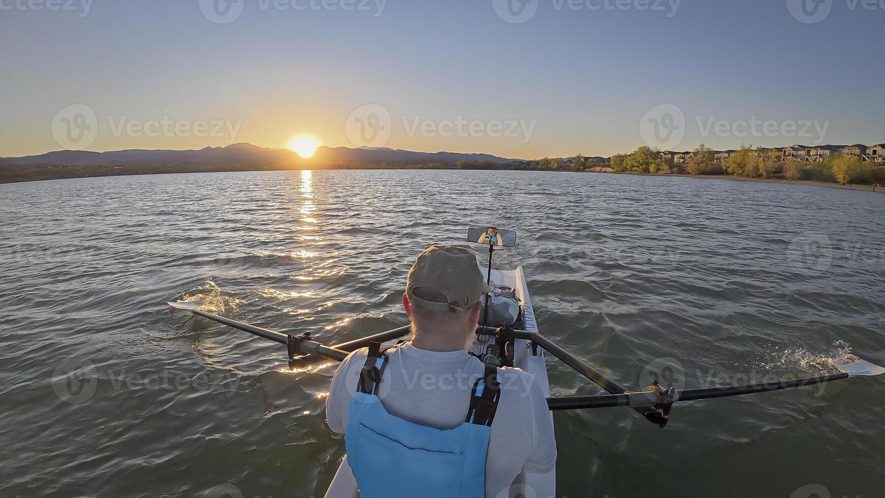 senior rower in coastal rowing shell on lake at Colorado foothills, spring sunset scenery photo