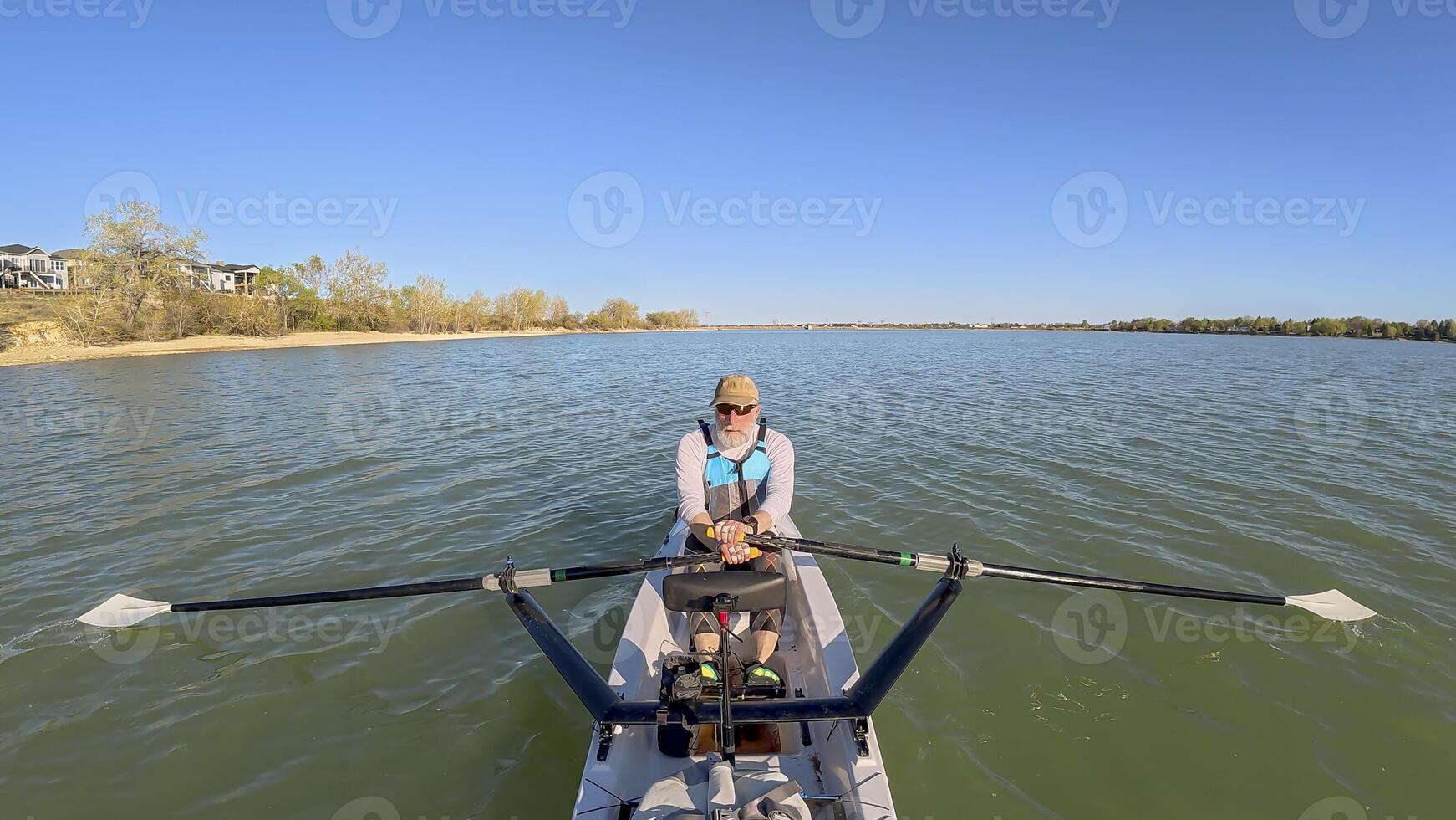 senior rower in coastal rowing shell on lake at Colorado foothills, spring scenery photo
