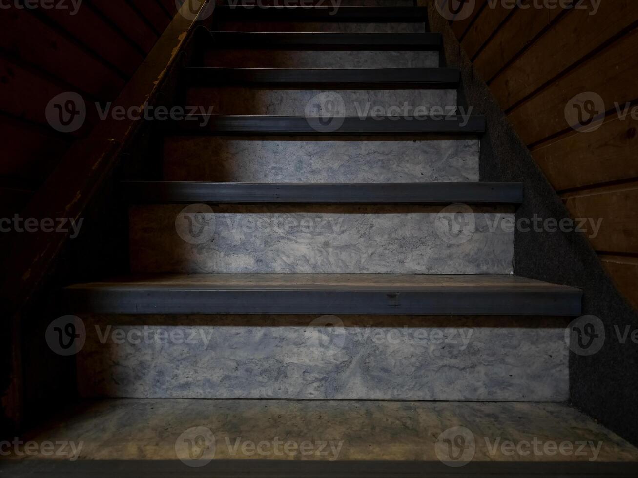 An eye-level perspective of a wooden staircase with textured steps and dark shadows. photo