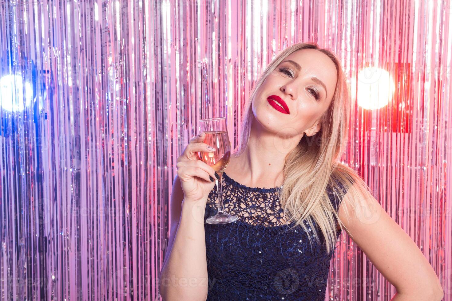 Party, drinks, holidays and celebration. Smiling woman in evening dress with glass of sparkling wine over shiny background. photo