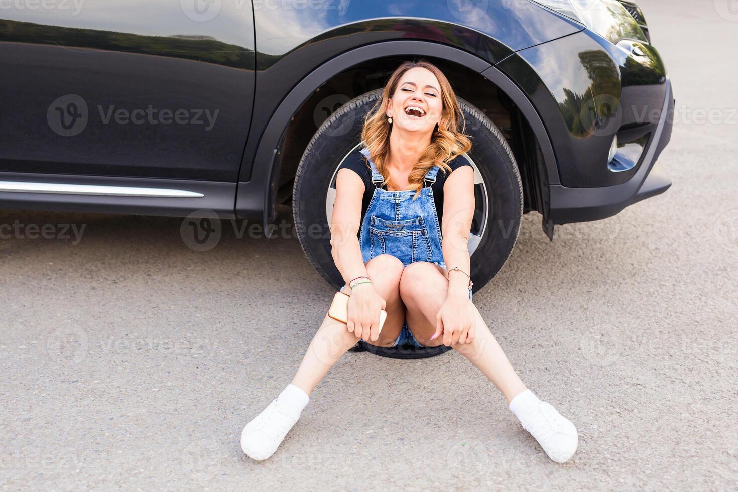 young woman sitting on road near car and laughs outdoor in sunny day photo