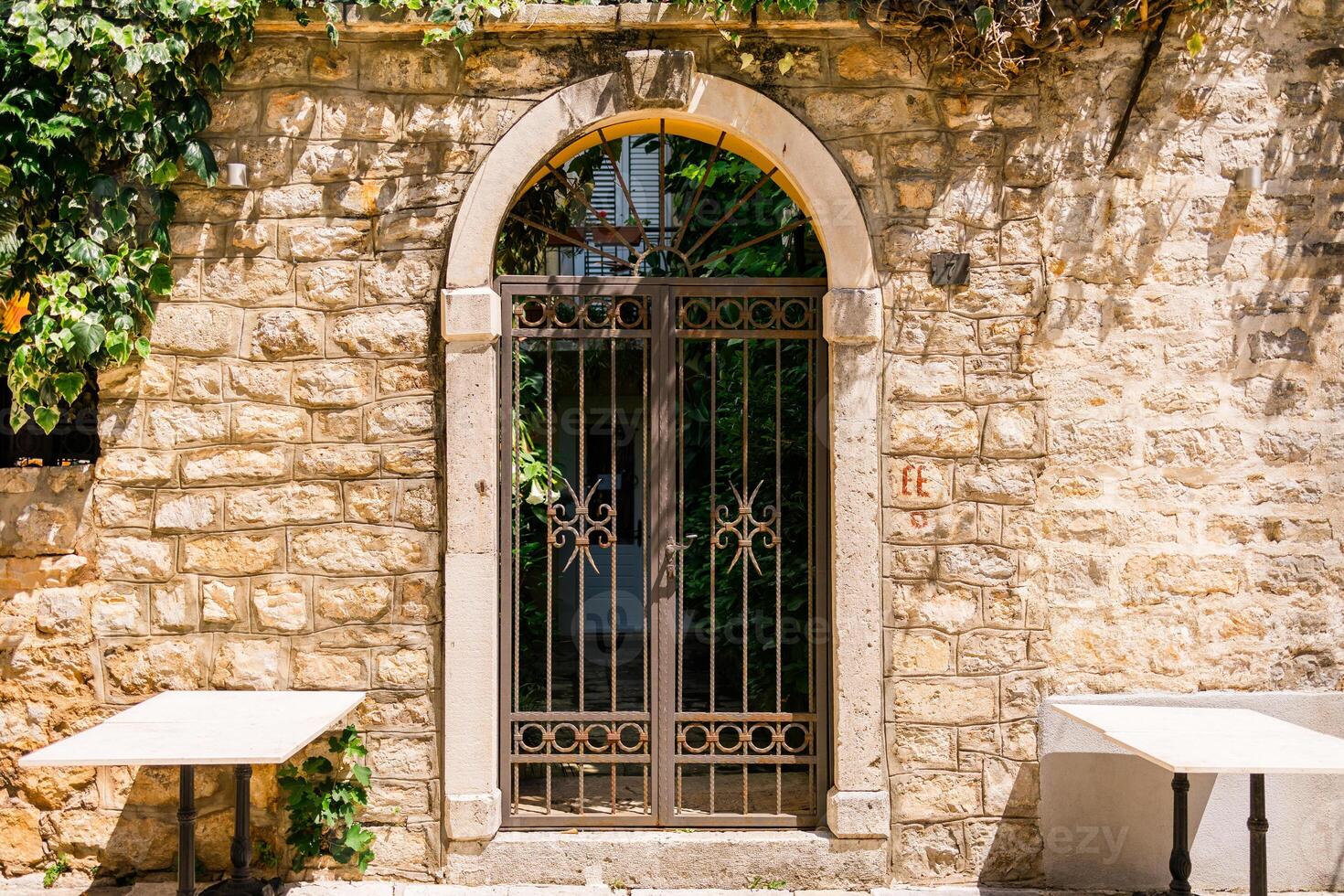 Iron gate set in stone wall under arched doorway. Mediterranean courtyard, vintage architecture and sunny outdoor charm. photo