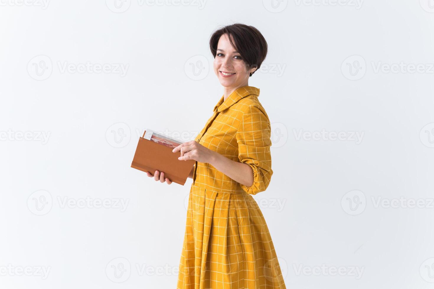 Portrait of a beautiful brunette girl in a yellow retro dress reading a book on white background. with copy space. photo