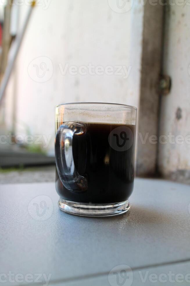 a glass of a black coffee in a glass cup photographed from the side, during the day photo