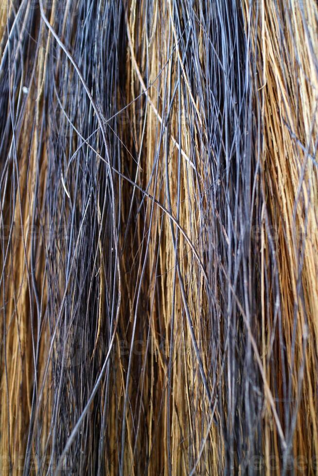 The textured fibers of a coconut broom, woven in a striking pattern of yellow and black, create a vibrant contrast against the rustic handle photo
