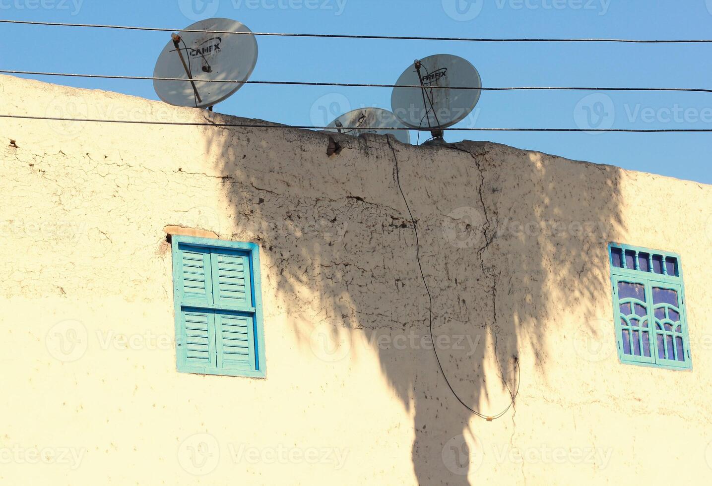 Wall of an old house with palm trees shadow and satellite dishes on rooftop. photo
