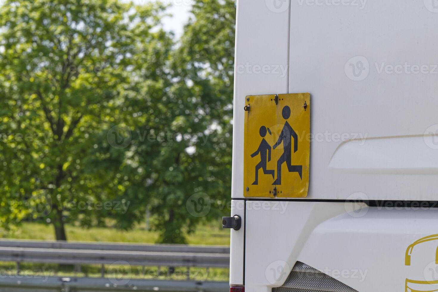 A yellow and black sign at the rear of the school bus warns of running students photo
