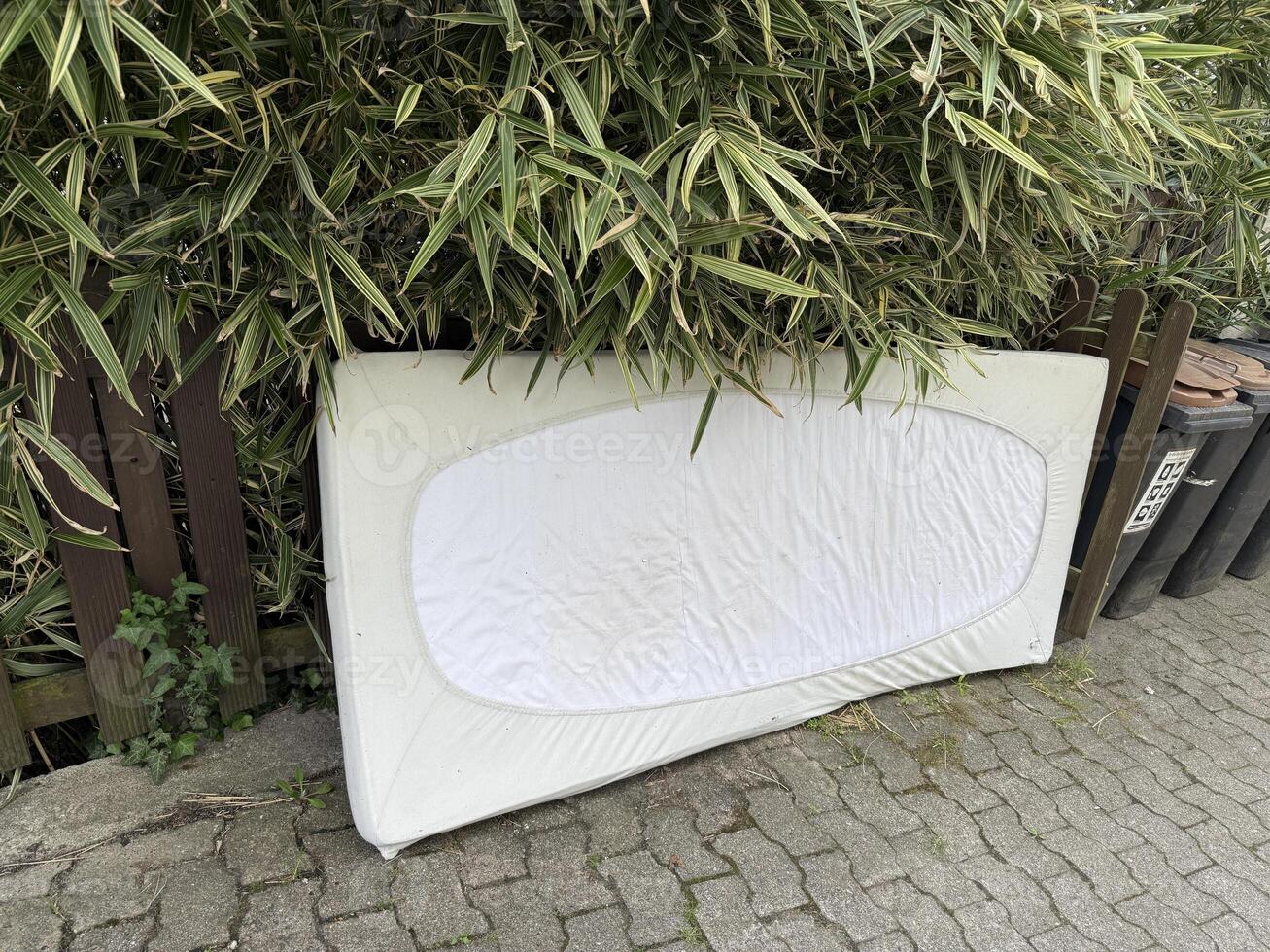 A mattress with fitted sheets was temporarily stored outside for disposal photo