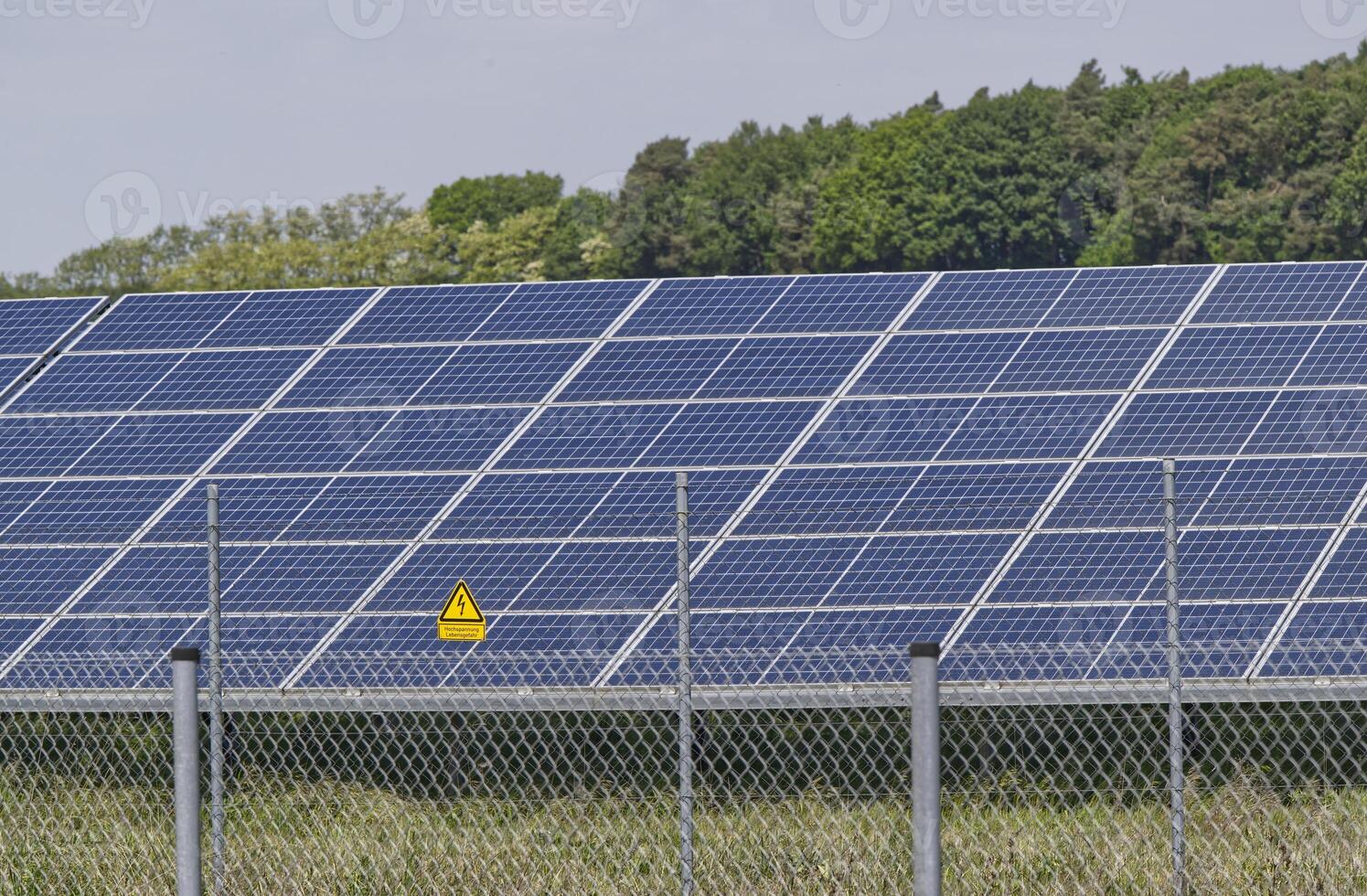 A Northern German solar farm, a field full of solar panels is protected by a fence with a warning sign photo