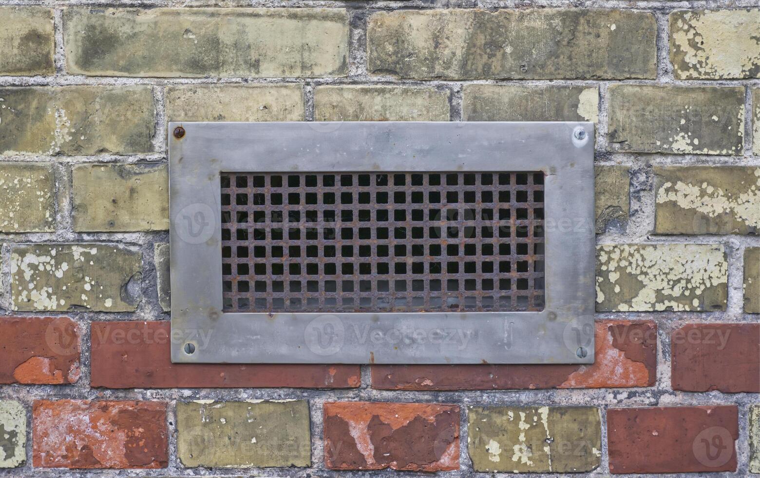 A rusty metal grid is built into a wall, which has a wide steel frame photo