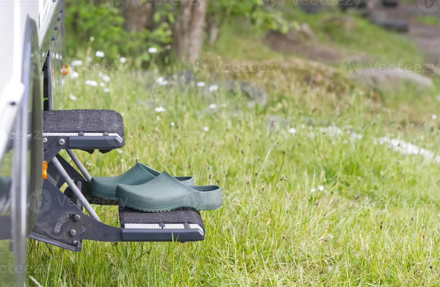 On the steps in front of the entrance of a camper there are green leisure garden shoes clogs in green photo