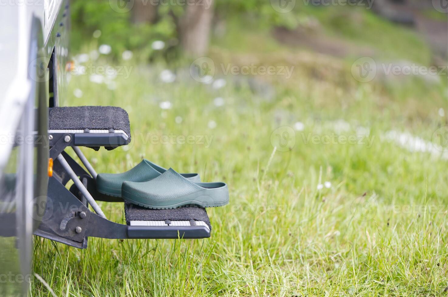 On the steps in front of the entrance of a camper there are green leisure garden shoes clogs photo