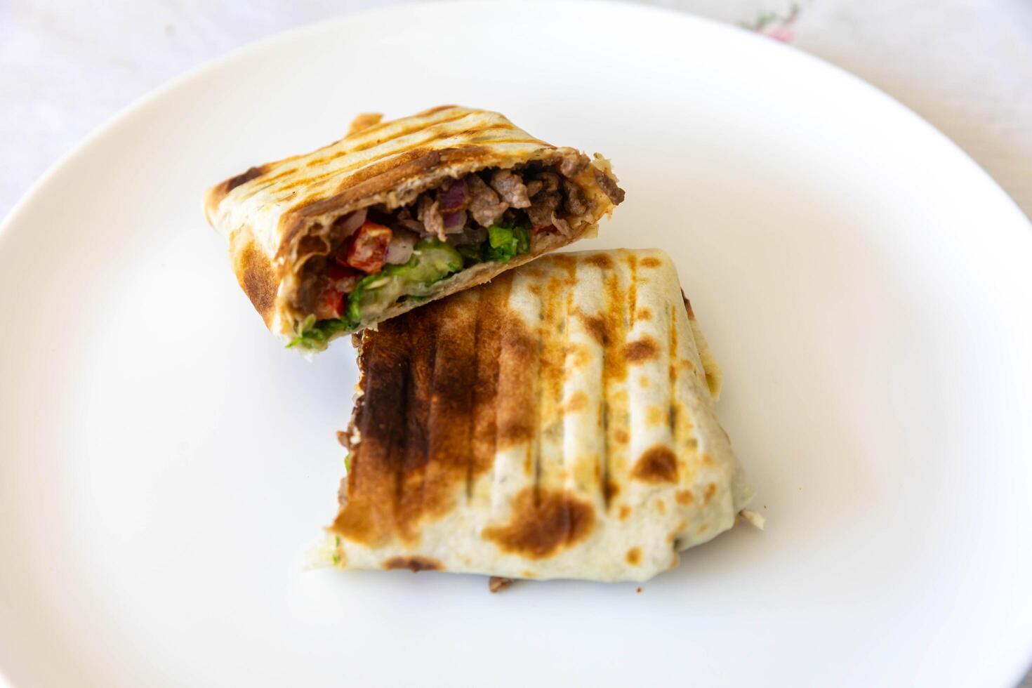Close-up of a delicious shawarma wrap held in hand on white plate photo
