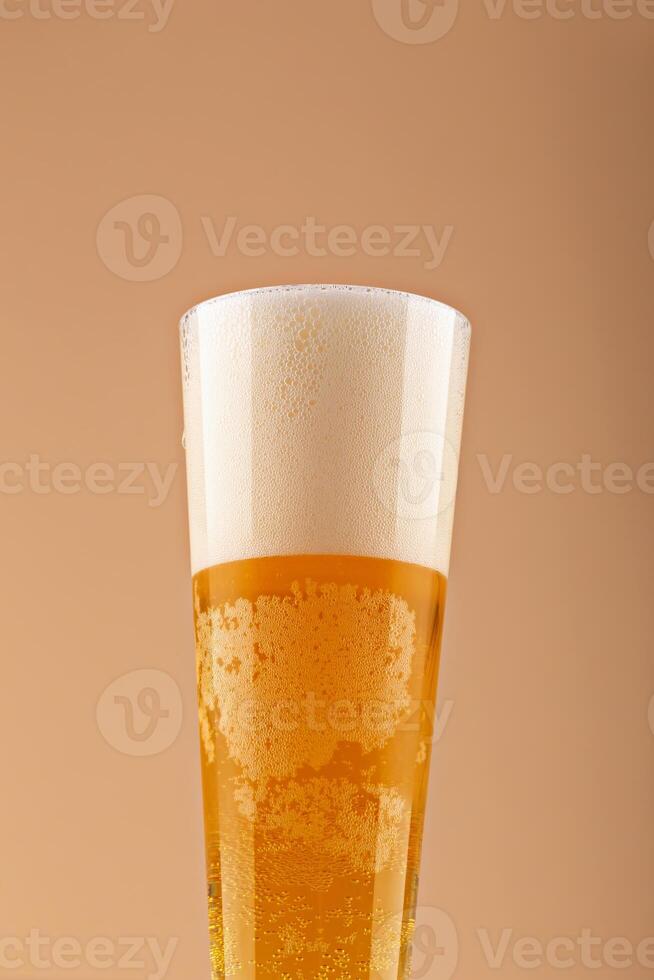 Close-up of frothy beer glass with golden bubbles rising under creamy foam against warm beige background. Concept of beer freshness and lager texture. Beer with thick foam and bubbles photo