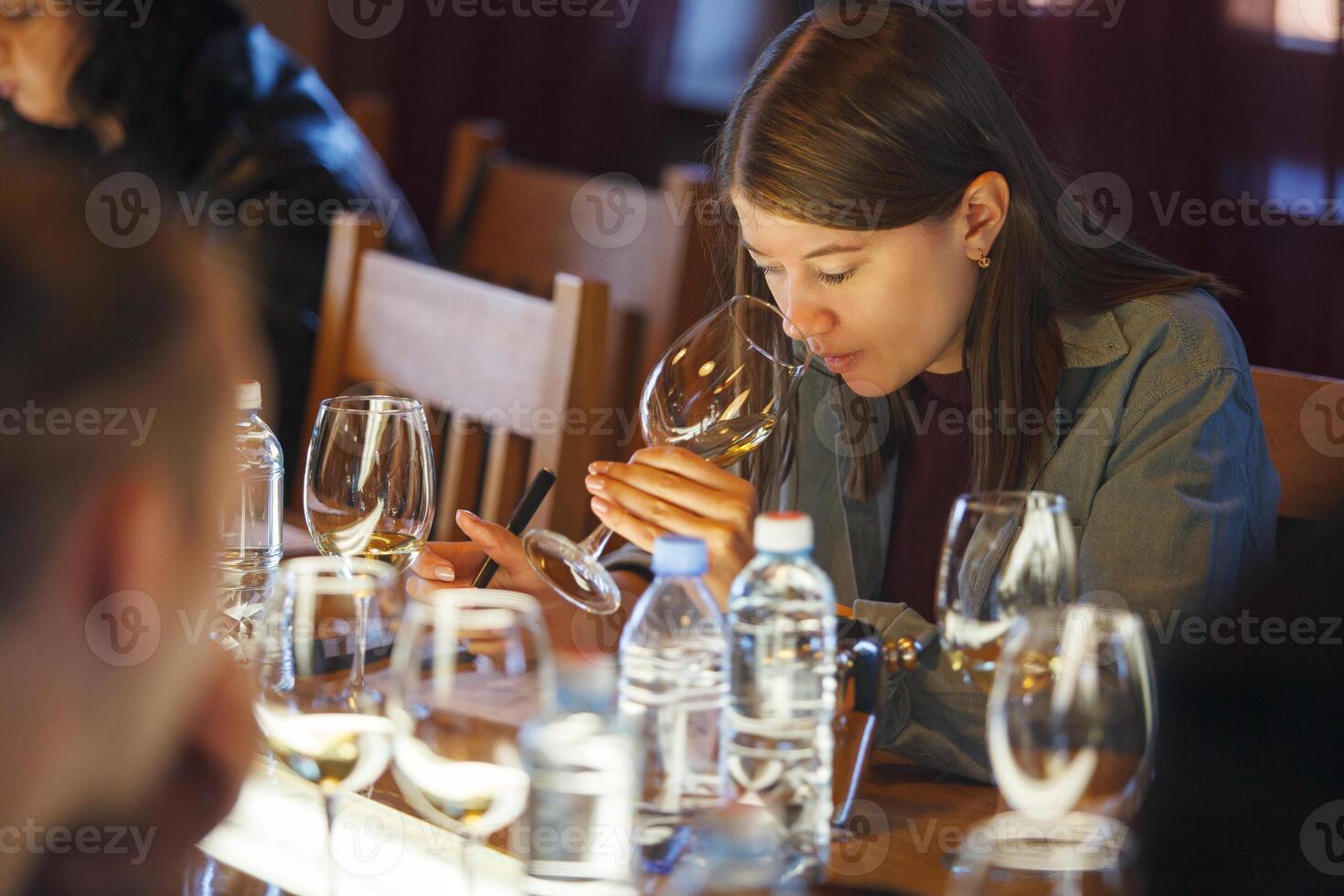 Woman Sitting at Table With Glass of Wine and Tasting White Wine photo