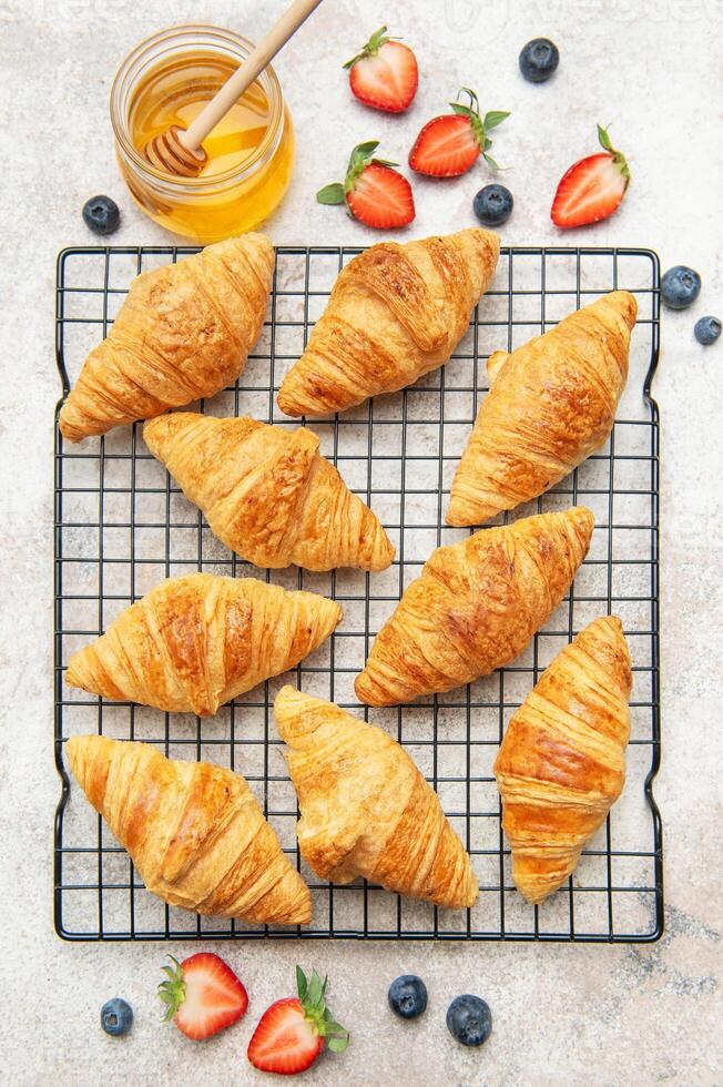 Freshly croissants cooling on a wire rack with honey and berries photo