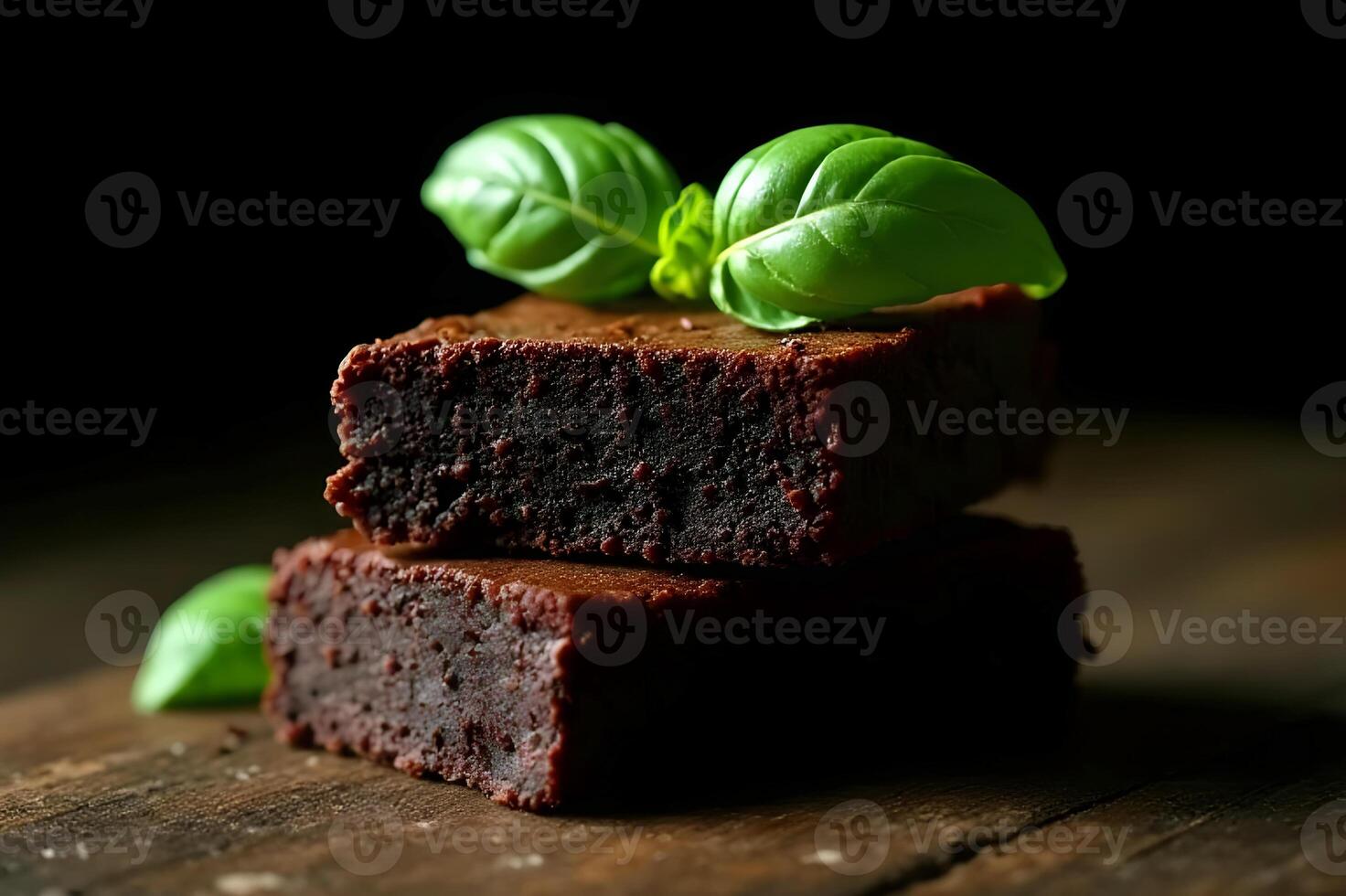 Two delicious chocolate brownies stacked and garnished with fresh basil leaves on rustic wood photo