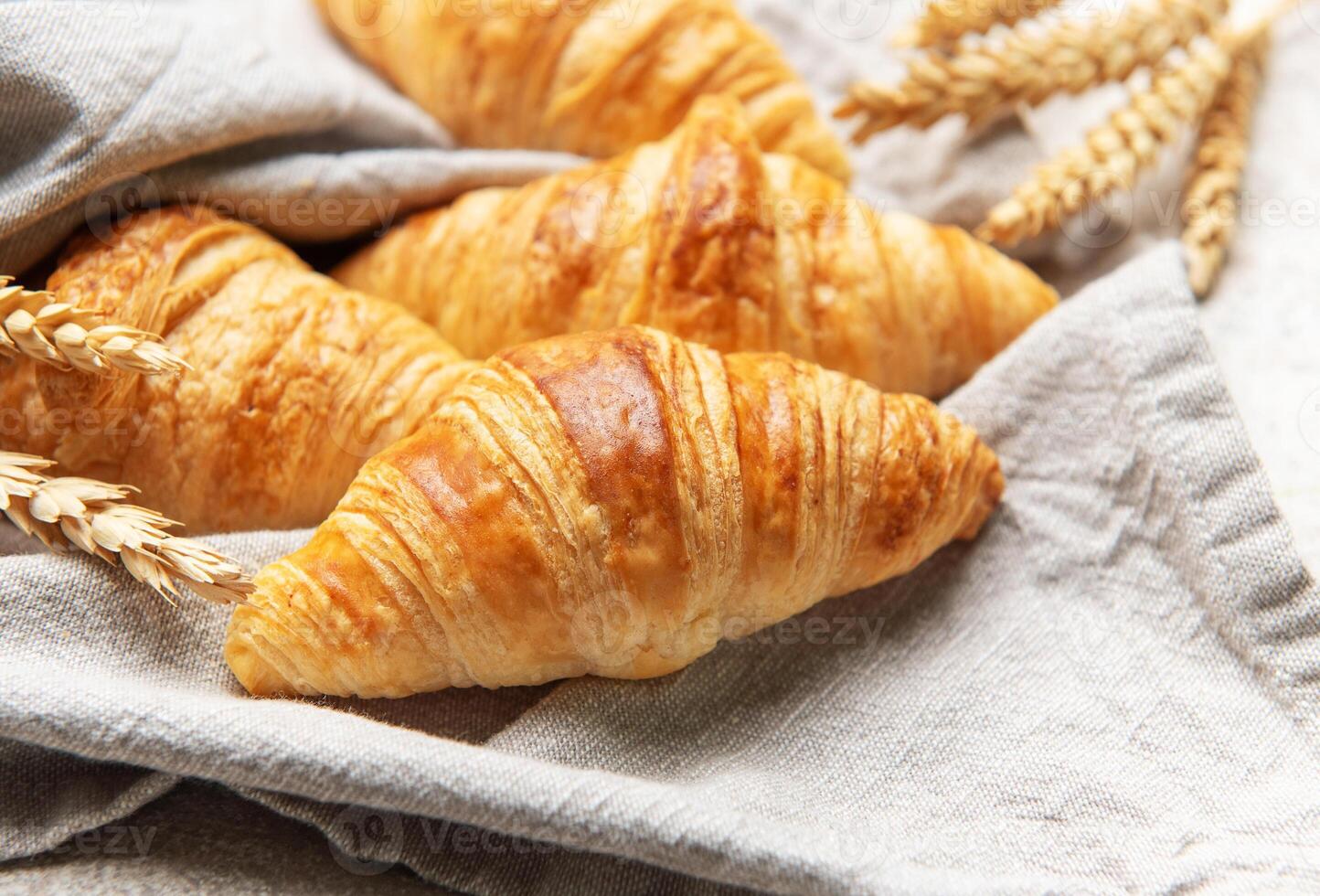 Freshly baked croissants resting on a linen cloth with wheat stalk photo