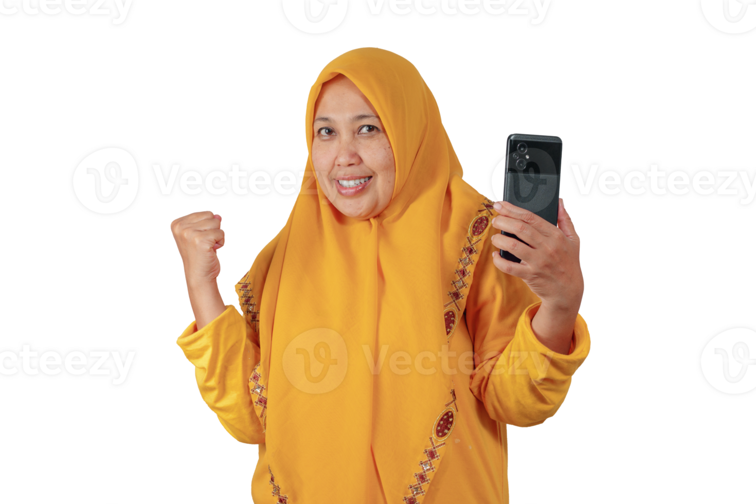 Middle aged woman in yellow hijab smiling and raising fist with smartphone in hand png