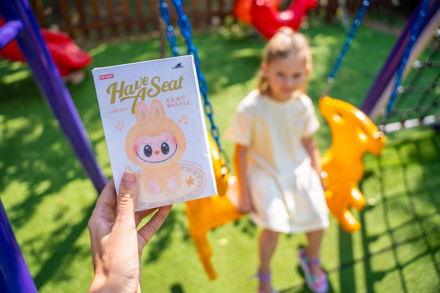 Budva, Montenegro - June 12, 2025. Hand with boxed LaBubu toy, one of the most popular collectible figures. Child waiting eagerly in background to receive trending gift. photo