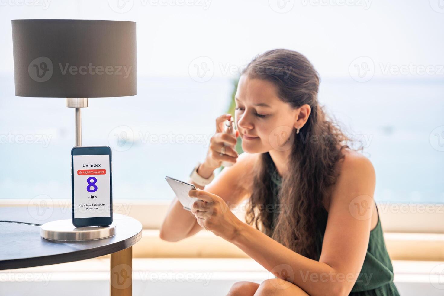 Smartphone with high UV alert in focus, while woman applies sunscreen to her face in mirror. Conscious skincare routine inspired by sun safety warning. High quality photo
