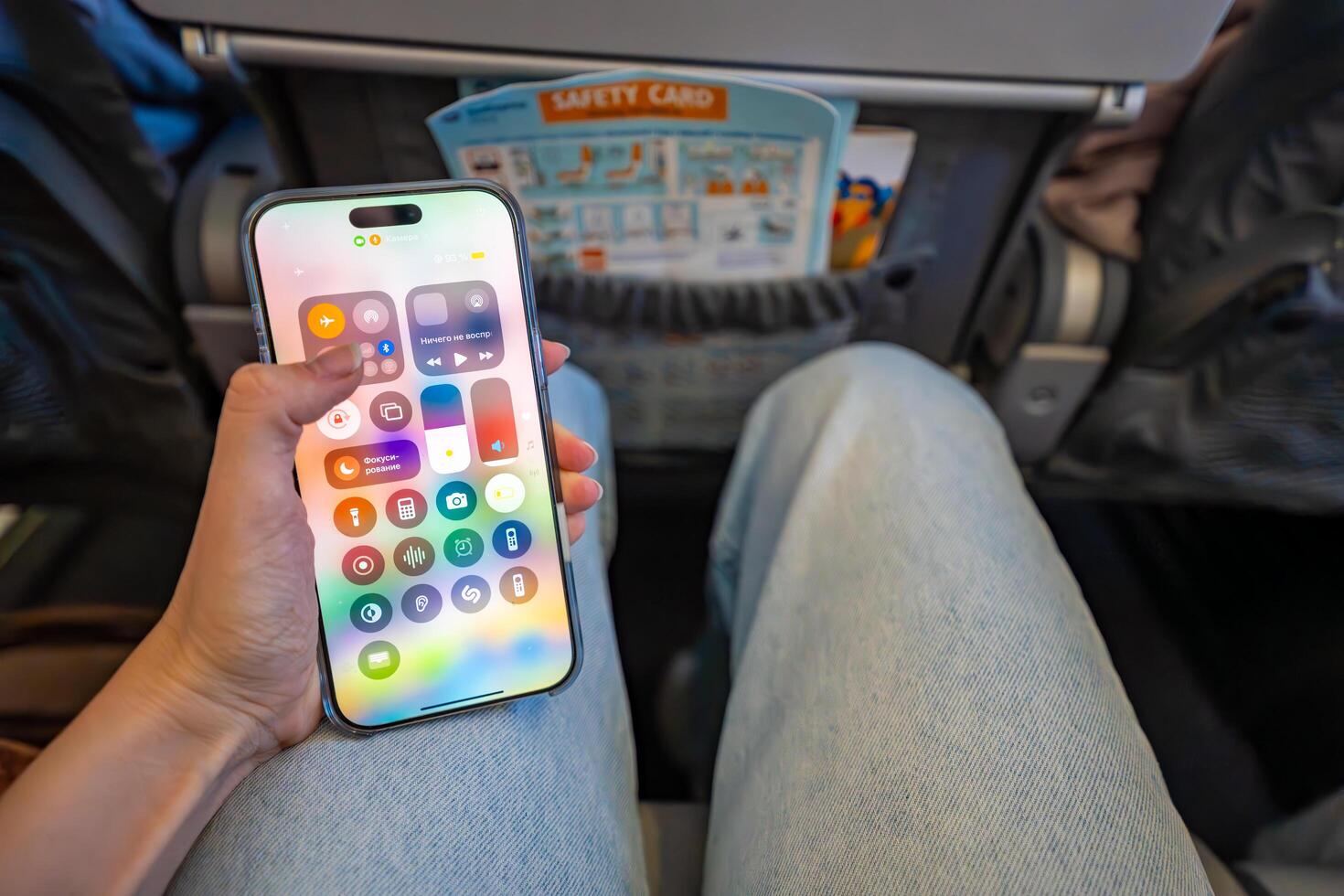 Prague, Czech republic - May 7, 2025. Woman activating airplane mode on iPhone while seated on plane before takeoff. Digital disconnection and travel preparation routine during flight. photo