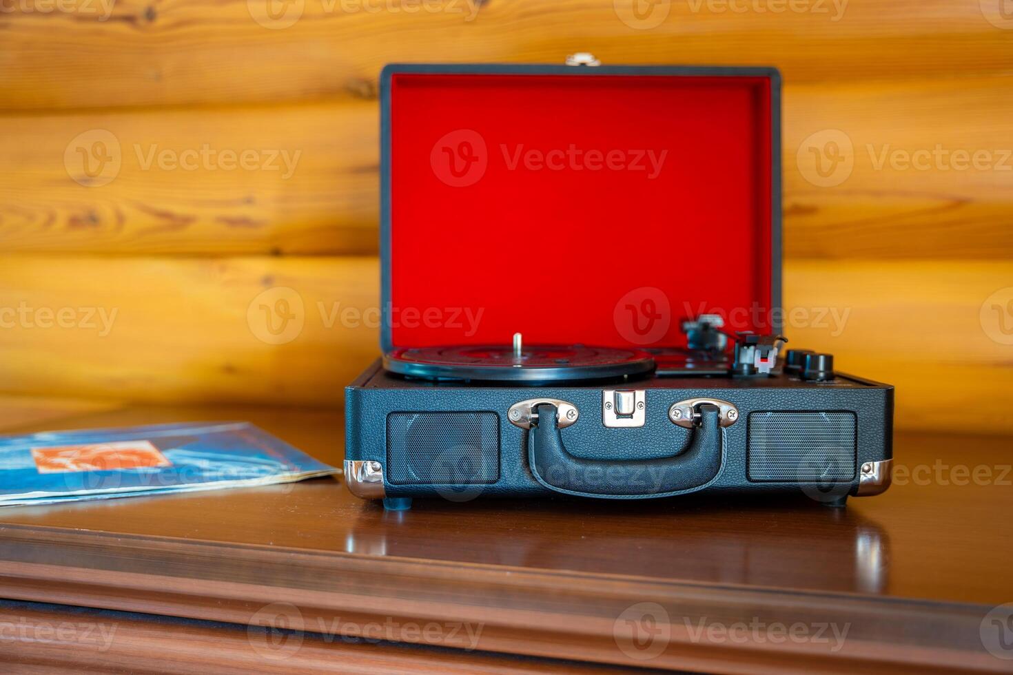 Open vintage record player in suitcase design with vinyl lying nearby. Retro music setup ready for playback in warm, nostalgic atmosphere. High quality photo