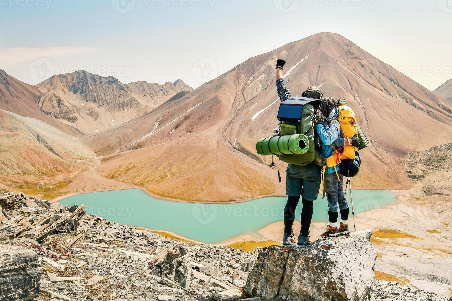 caucasian adult hikers together stand hugging caring on top mountain enjoy panorama. Man and woman standing and hugging on the top of the mountain, autumn hike with backpacks.Alpine Kelitsadi lake. photo