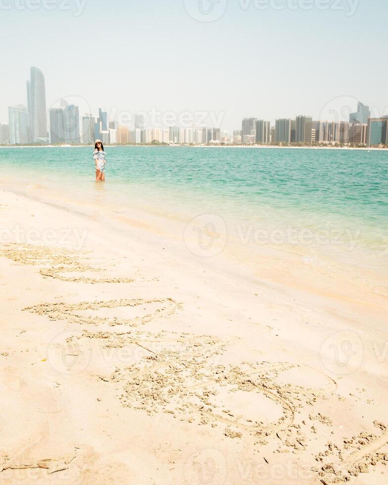 Happy young female tourist on viewpoint in hot day visiting Abu dhabi, UAE - Traveller girl taking portrait in front of capital skyline background. Urban middle east city life travel attractions. photo