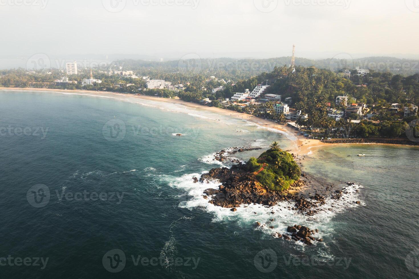 Aerial top down view Mirissa Beach and Parrot Rock, showcasing pristine turquoise waters, golden sandy shores, rocky coastal formations, southern Sri Lanka. Vibrant tropical landscape indian ocean photo