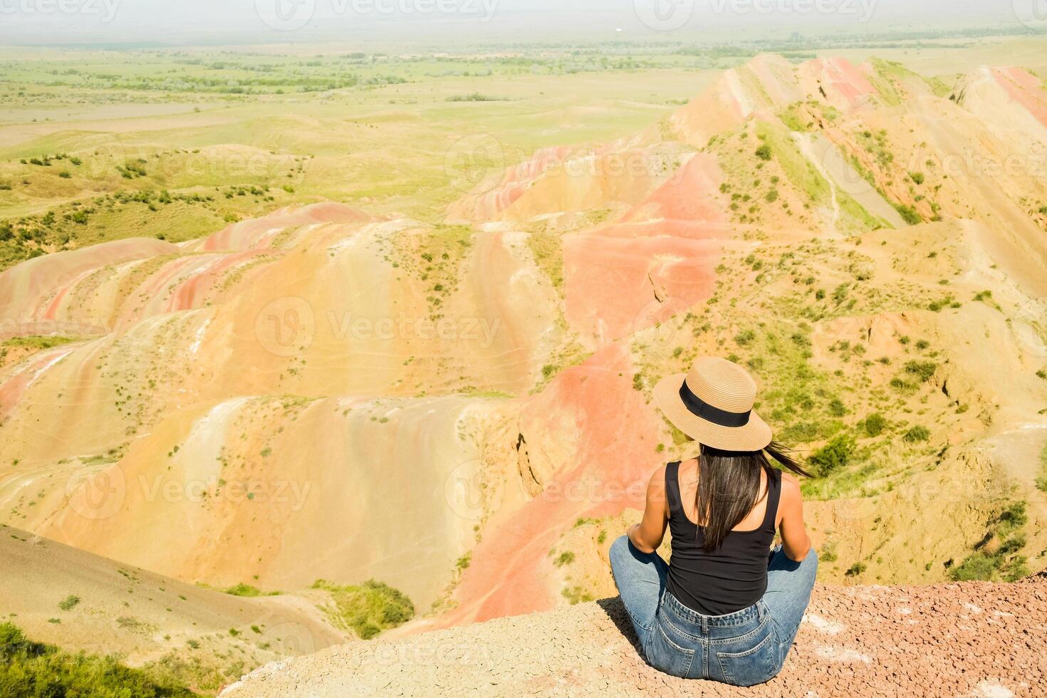 Woman tourist enjoy nature sit relax on colorful vibrant striped hills Mravaltskaro rainbow mountains, Georgia, with unique layered terrain expansive steppe background. Mravaltskaro Colorful Mountains photo
