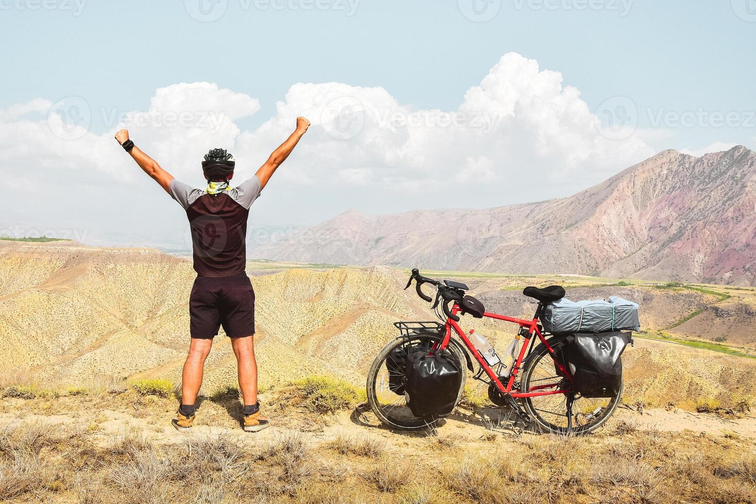 inspirational excited joyful caucasian male cyclist on viewpoint by red touring bicycle in deserted mountains with hands up confident carefree lifestyle photo