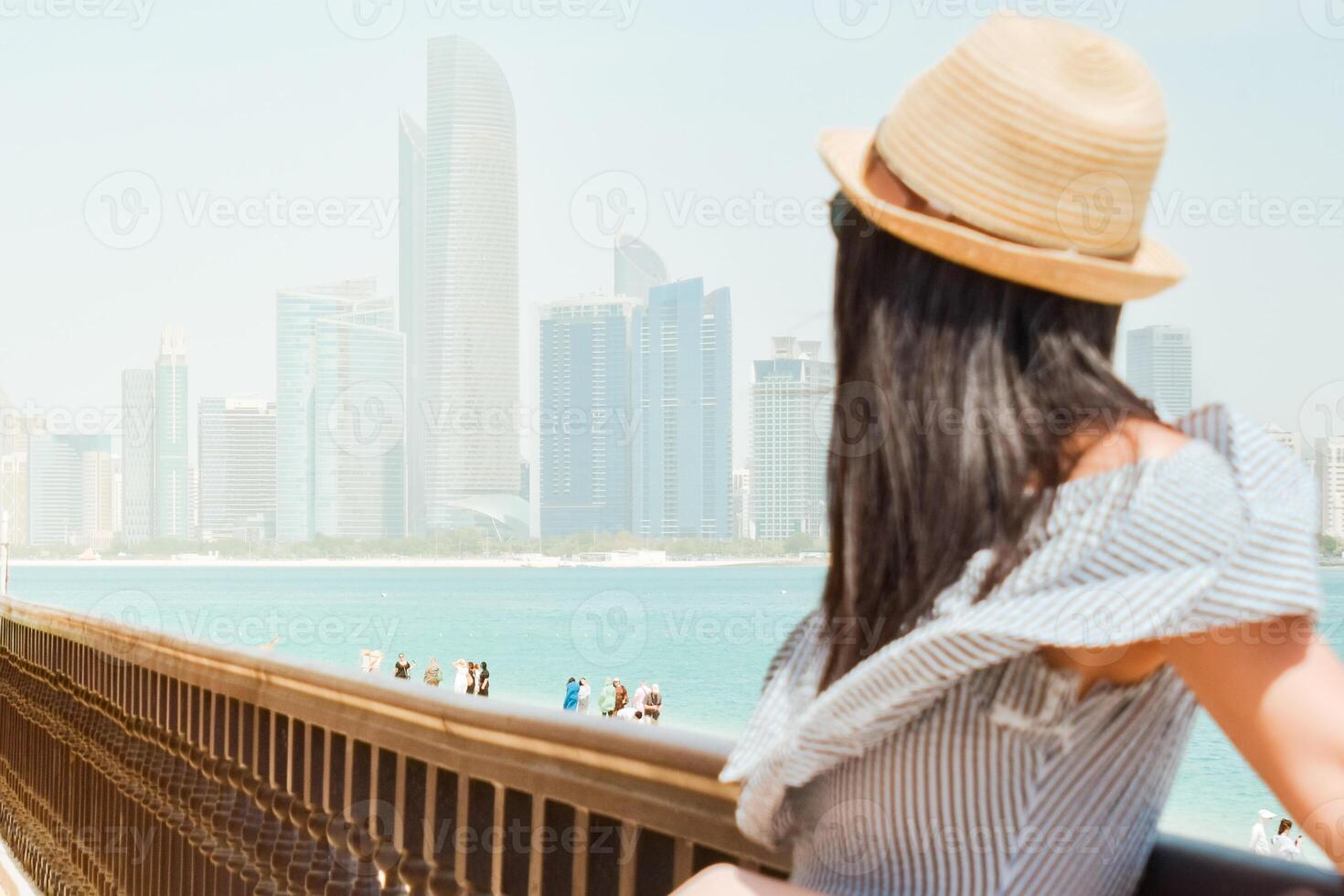 Portrait caucasian pretty tourist woman at viewpoint looking to Abu Dhabi skyline panorama and beach, reflecting peace, relaxation, and urban beauty in the UAE photo