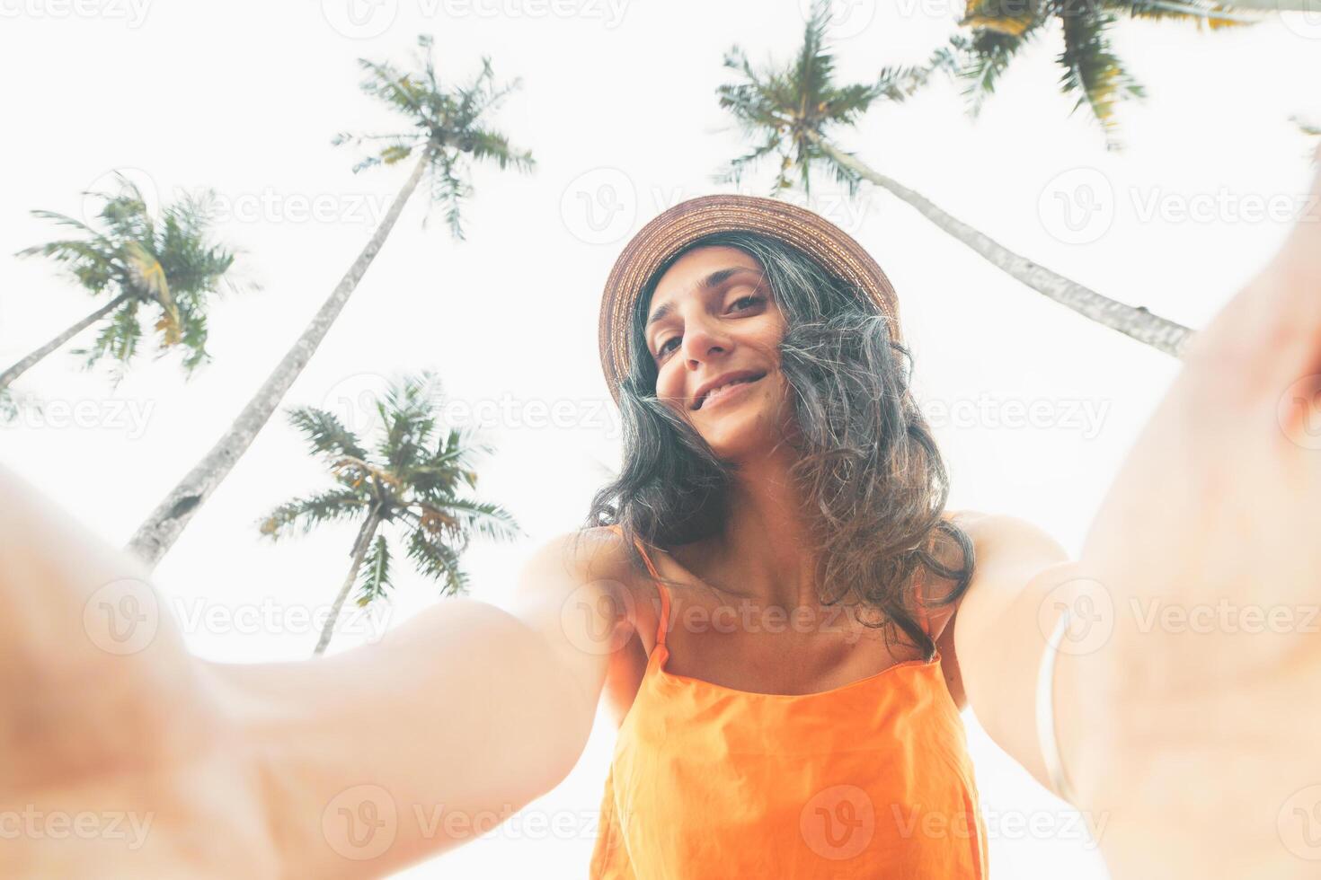 Natural caucasian woman in 40s pose selfie smile to camera on vacation in tropical island surrounded by palm trees and blue sky. Graceful Aging concept. Embracing Beauty, Wisdom, Confidence Over Time. photo
