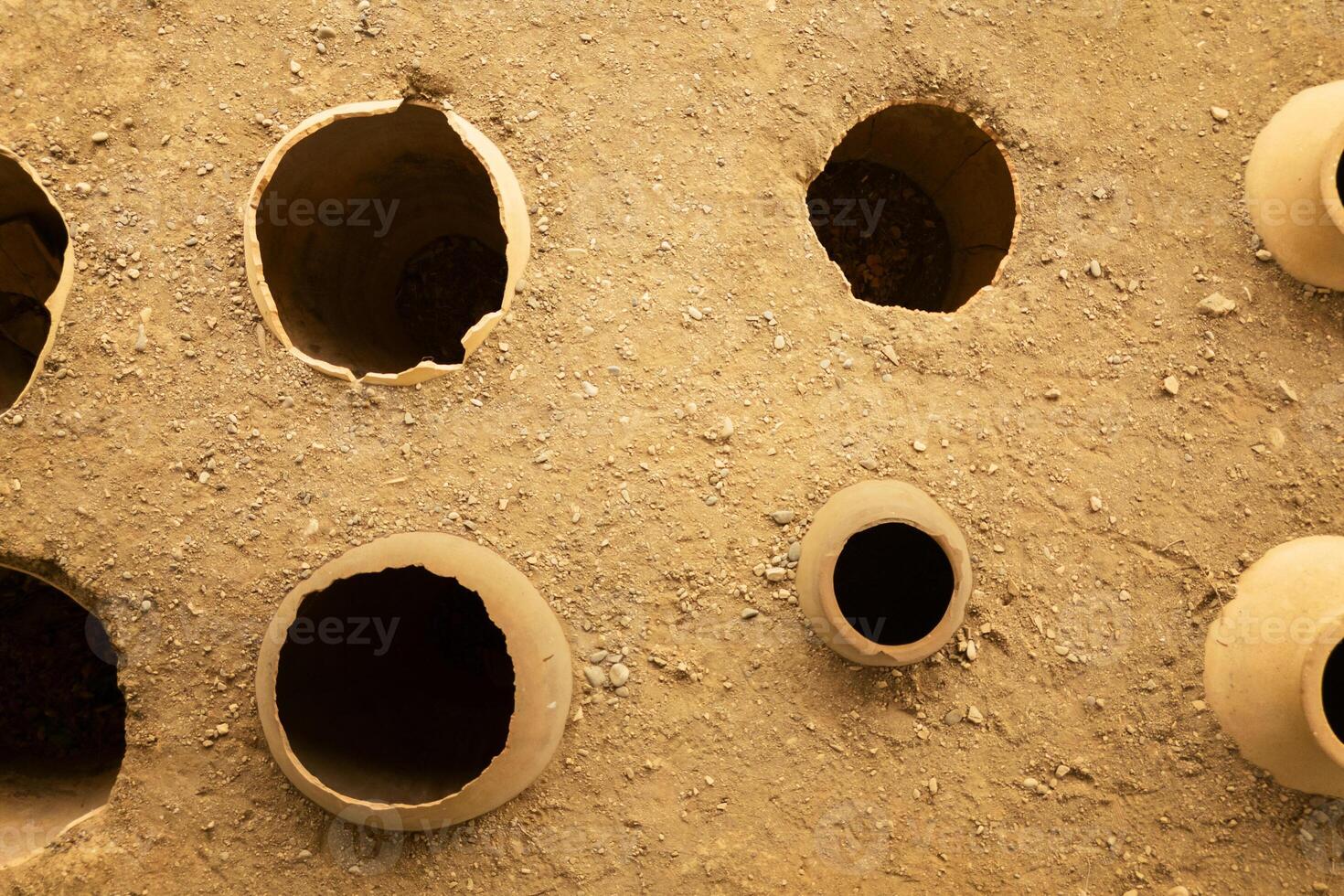 Clay wine vessels embedded earth beneath wooden shelter at Armaziskhevi site, part of an ancient wine making cellar in Mtskheta region, Georgia. photo