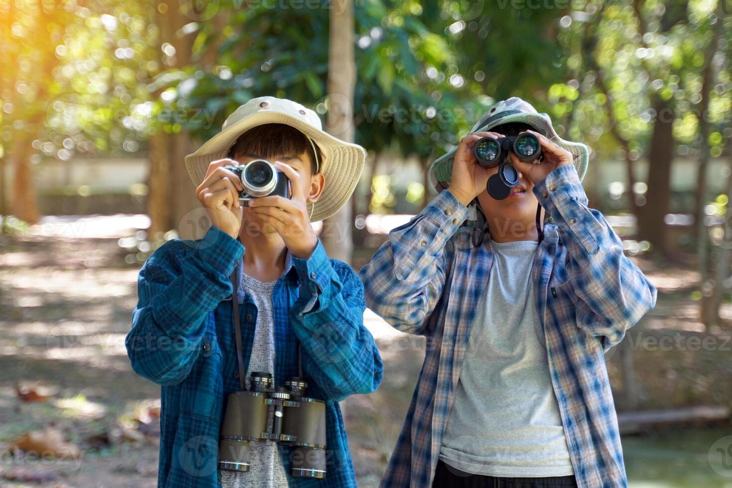 2 Asian boys use binoculars and a camera to study the local birds in a community forest. Soft and selective focus. photo