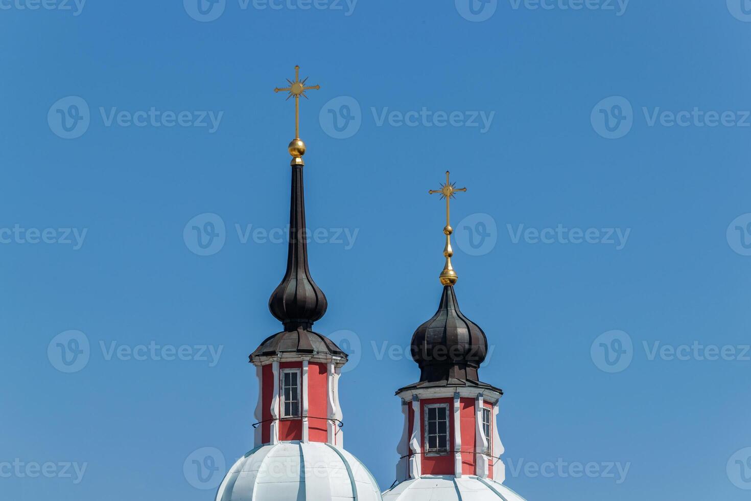 Two church towers with black domes and golden crosses of the cathedral against a blue sky background. photo