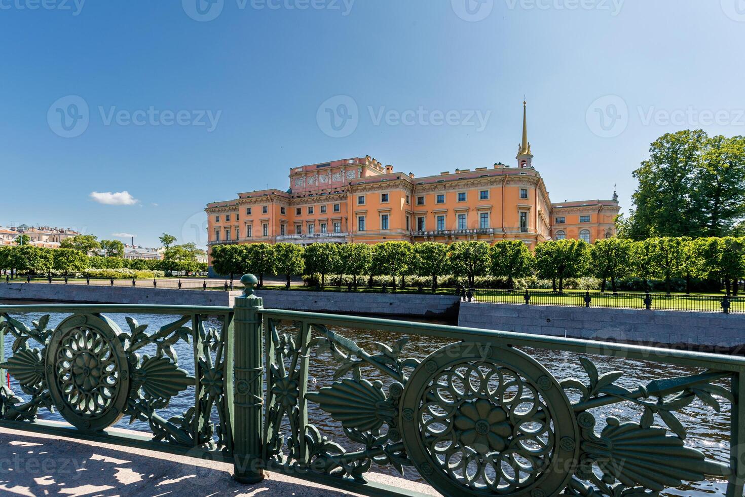Mikhailovsky Castle is visible behind an openwork bridge fence and a river under a blue sky. photo