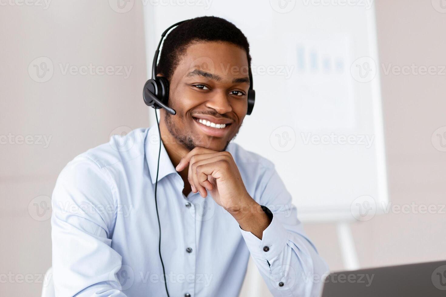Cheerful black guy worker call center representative with headset using laptop, smiling at camera, african american man having business training or conference online in office, copy space photo
