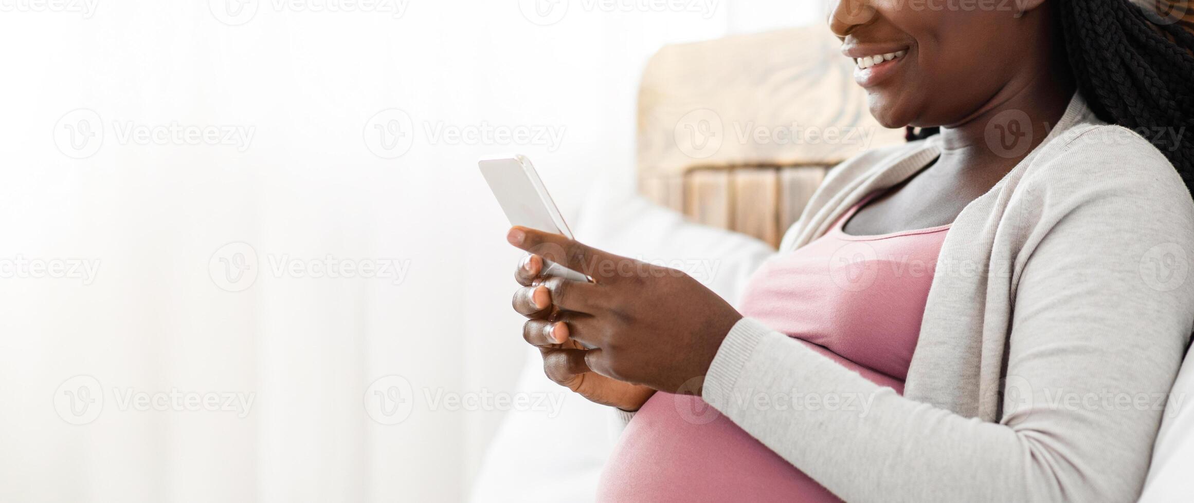 Joyful Black Pregnant Lady Spending Time With Smartphone At Home, Browsing Internet Or Messaging With Friends, African Expectant Woman Relaxing On Comfortable Bed, Side View Shot With Copy Space photo