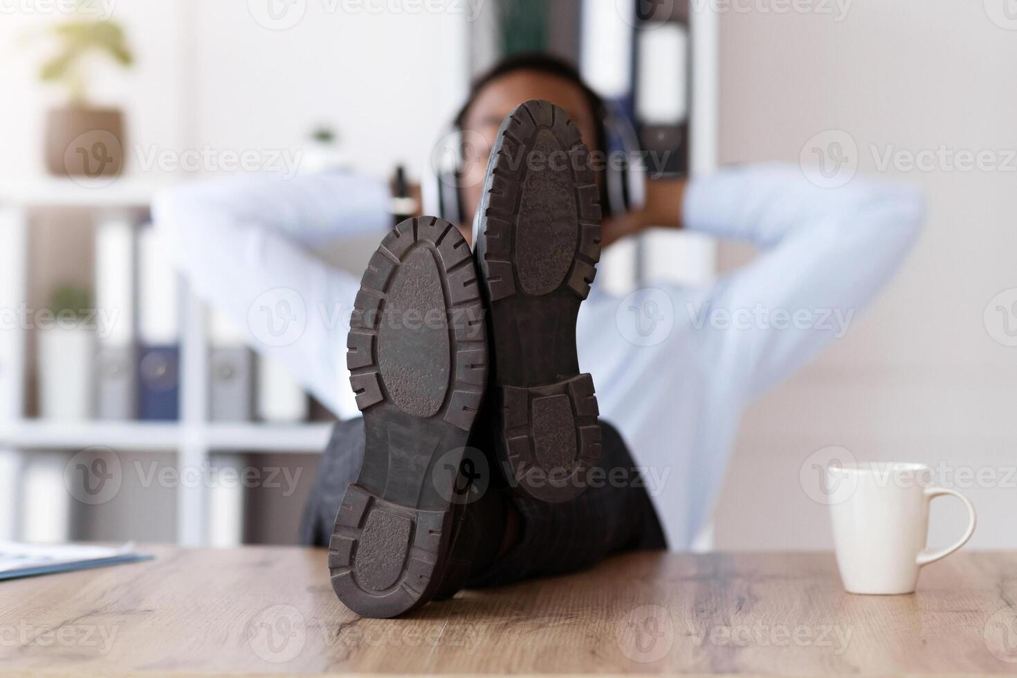 Resting black man shoes on workdesk in office, african american young businessman with headphones listening to music, leaning back, manager relaxing after difficult working day, empty space photo