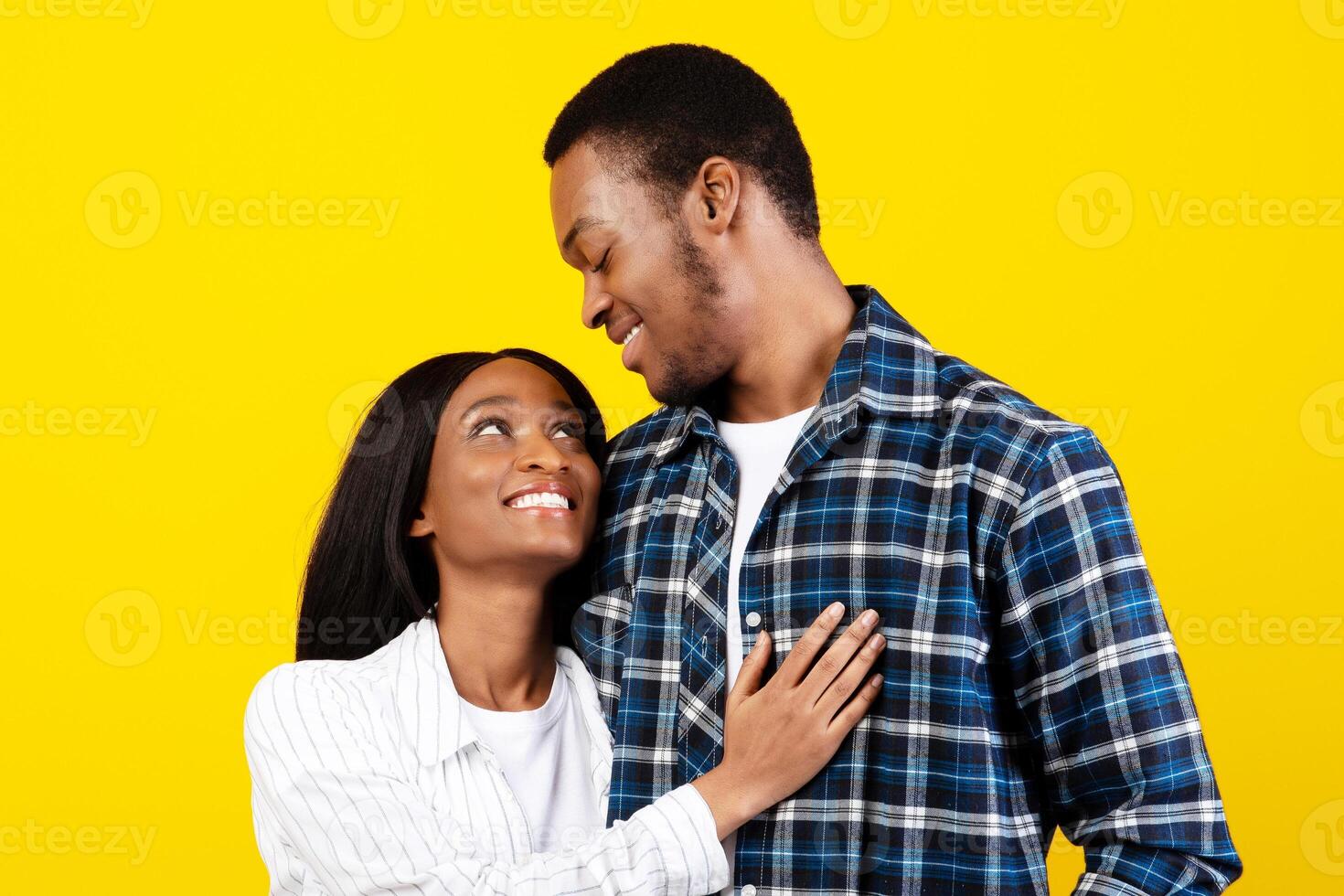 Tender moment, young romantic couple enjoying, married people have fun at date. Happy african american guy and lady hugs and looks at each other, isolated on yellow background, studio shot, free space photo