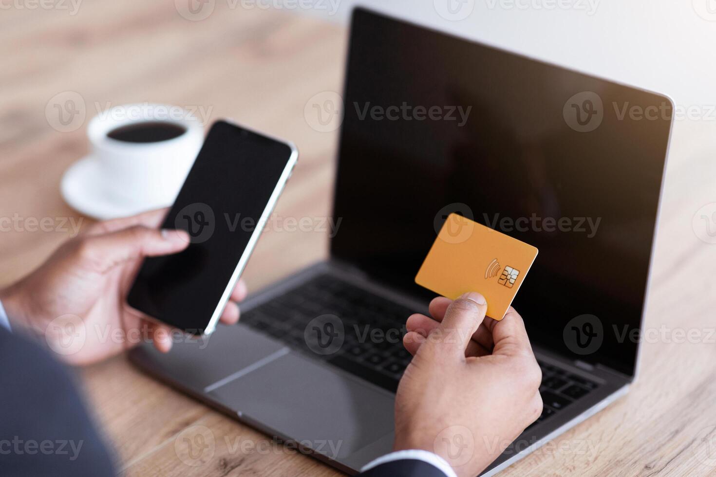 Closeup of unrecognizable african american businessman using mobile phone and modern laptop with empty screens, holding credit card, shopping online from his office, cropped photo