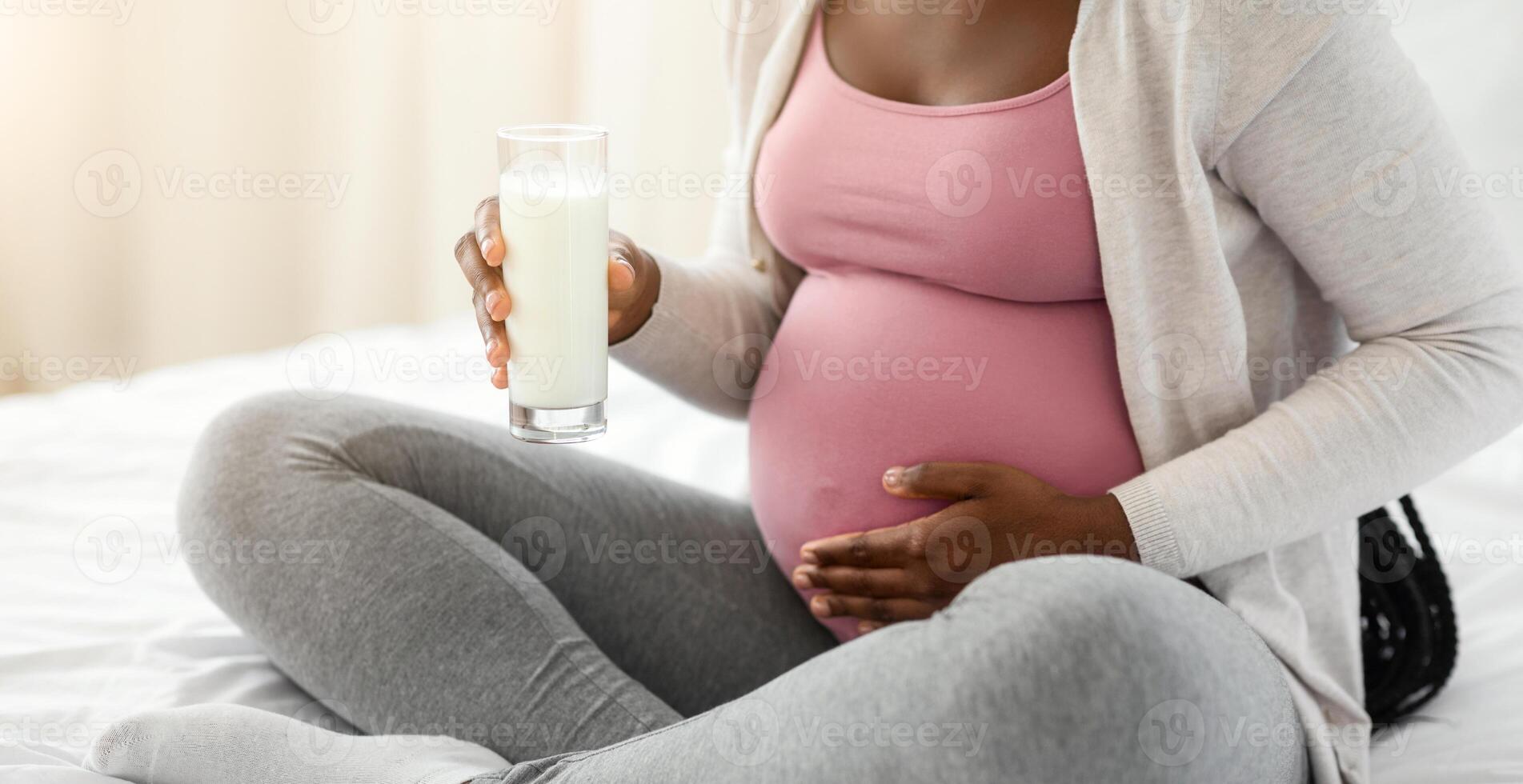 Pregnancy Nutrients. Unrecognizable Black Pregnant Woman Holding Glass With Milk While Resting On Bed, African Lady Drinking Rich Calcium Beverage And Touching Belly, Cropped Image With Free Space photo