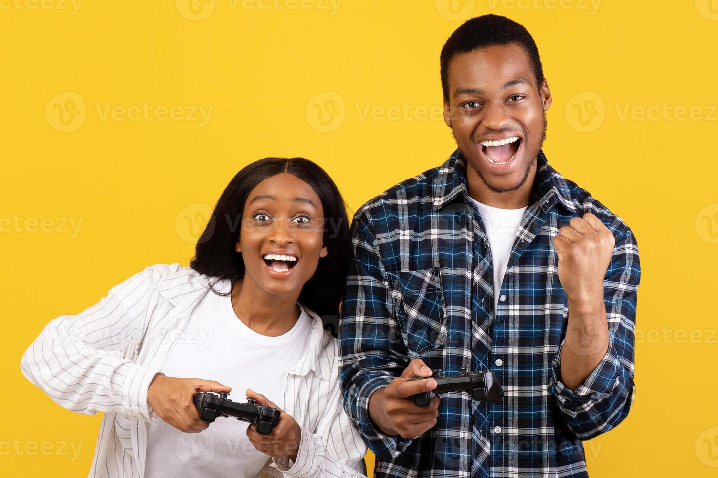 Have fun in free time together. African american young couple express emotions of success and play with joystick in online game, isolated on yellow background, studio shot, copy space, cut out photo