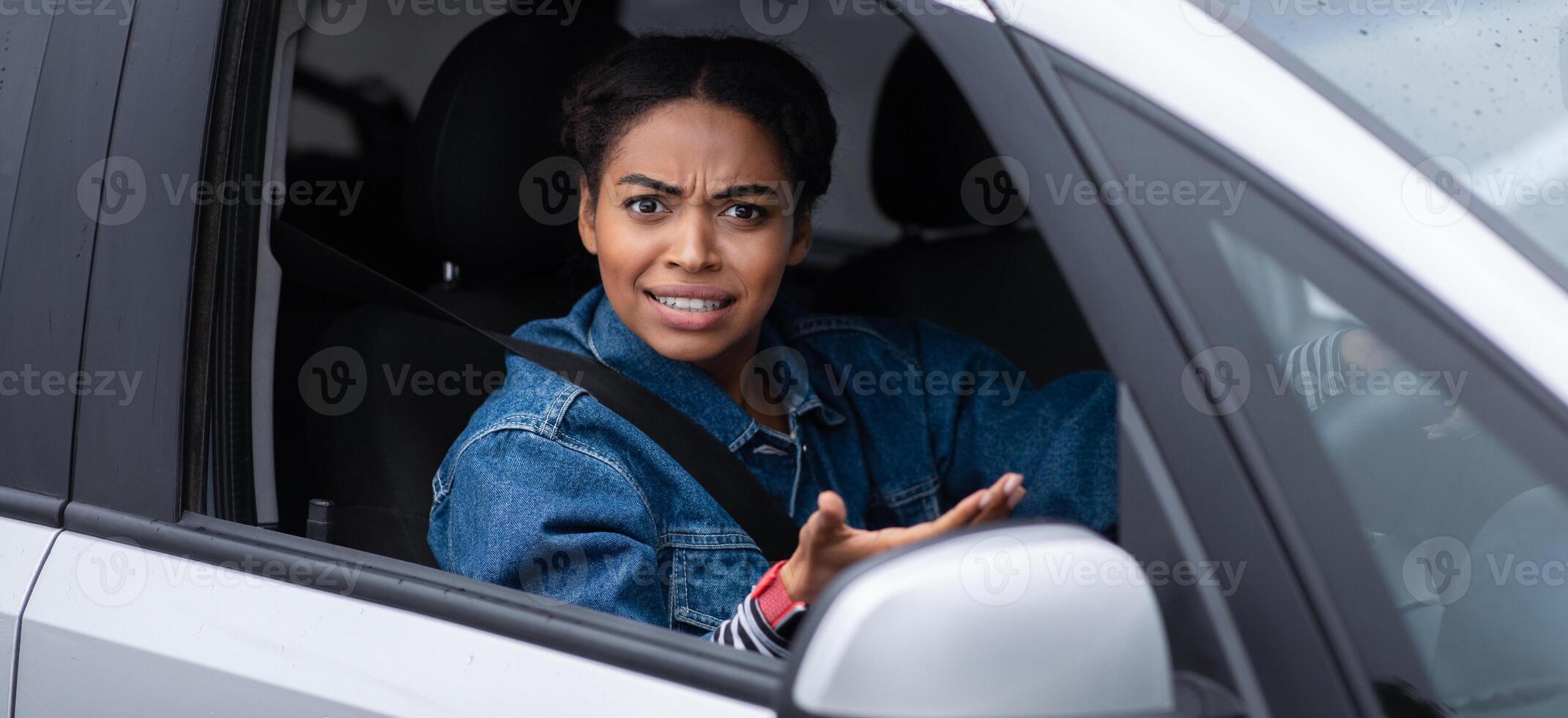 Conflict, difficulties and problems on city road. Excited angry millennial african american lady driver holding steering wheel, pointing at camera and looking out window and swears in car, side view photo