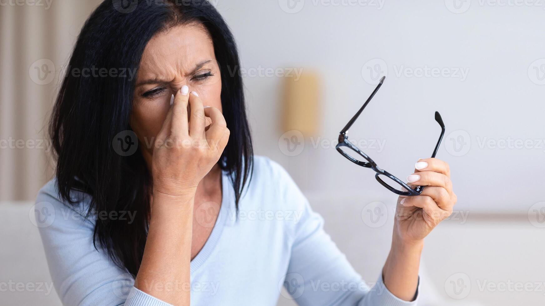 Stress From Work. Frustrated mature lady feeling tired, massaging nose bridge, suffering from eyestrain, holding specs. Having eyesight problem working on laptop at home in living room photo