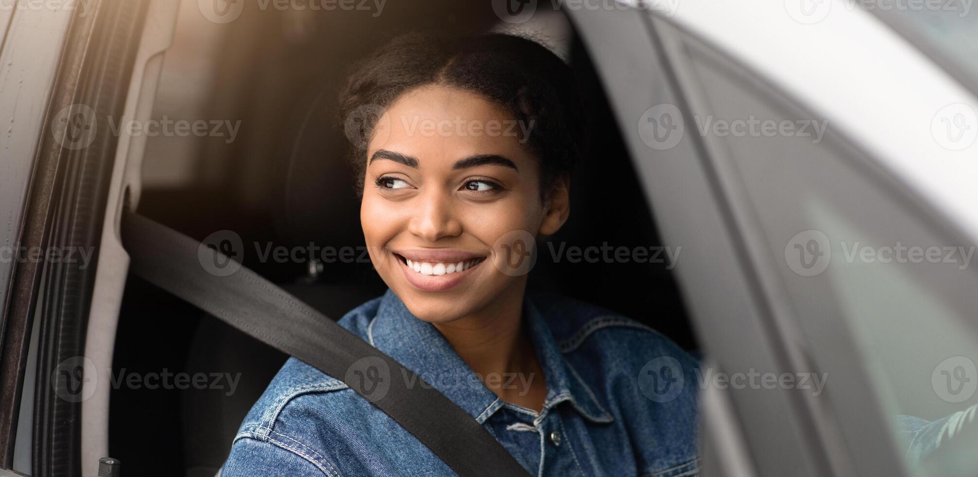 Meeting with friend on road in city, friendly taxi driver or flirt at traffic in town. Smiling millennial african american lady with seat belt looking outside window to another car, copy space photo